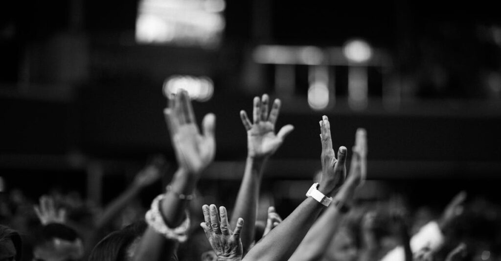 A group of people raising hands in a black and white concert setting, showing unity and celebration.